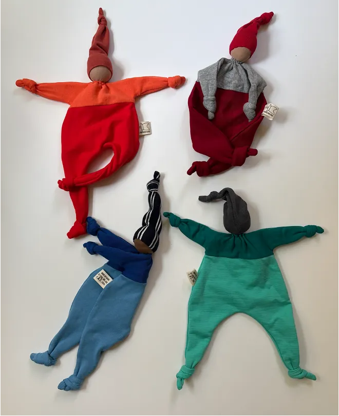 Four handmade loveys in red, blue and green laid out together.