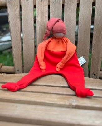 A red lovey with a pink hat sitting on a wooden chair.